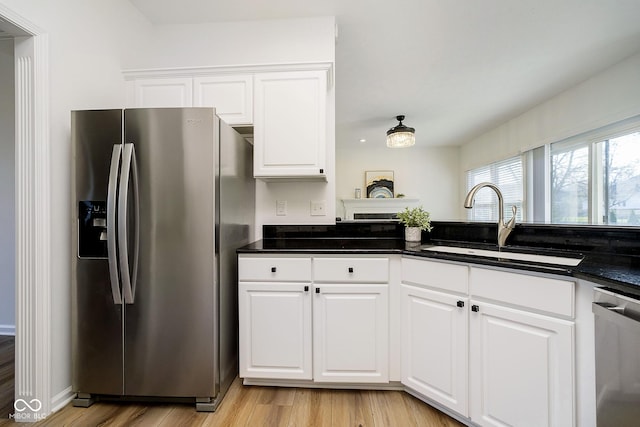 kitchen featuring white cabinetry, appliances with stainless steel finishes, dark stone counters, light hardwood / wood-style flooring, and sink