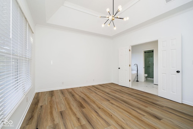 unfurnished bedroom featuring ensuite bath, wood-type flooring, a chandelier, and a raised ceiling