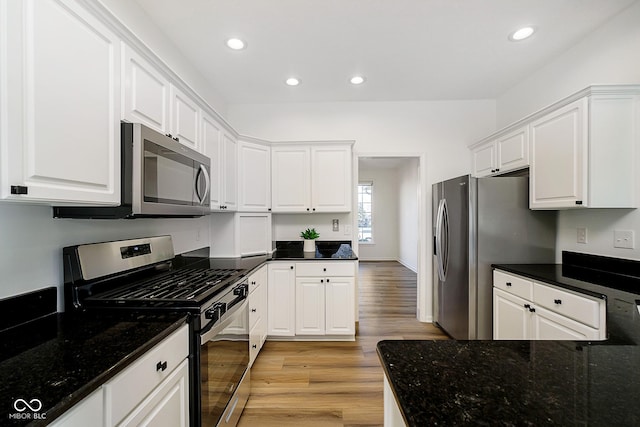 kitchen with white cabinets, light wood-type flooring, appliances with stainless steel finishes, and dark stone counters