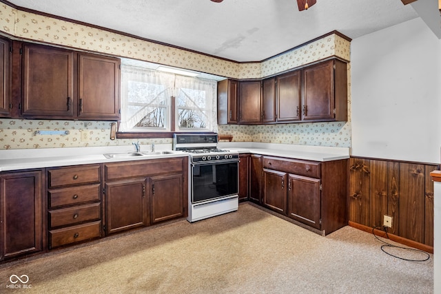 kitchen featuring a textured ceiling, wood walls, light carpet, and gas range gas stove