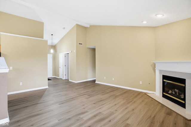 unfurnished living room featuring hardwood / wood-style floors, high vaulted ceiling, and a tiled fireplace