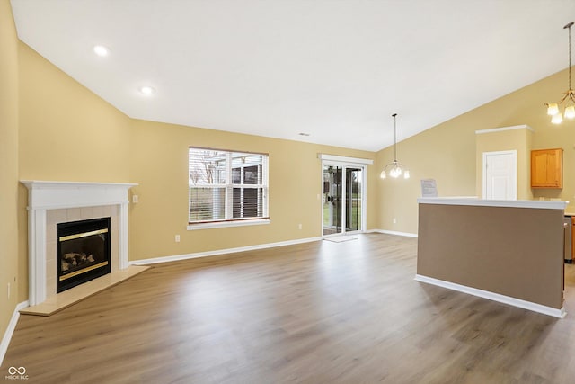 unfurnished living room with a chandelier, wood-type flooring, vaulted ceiling, and a tiled fireplace