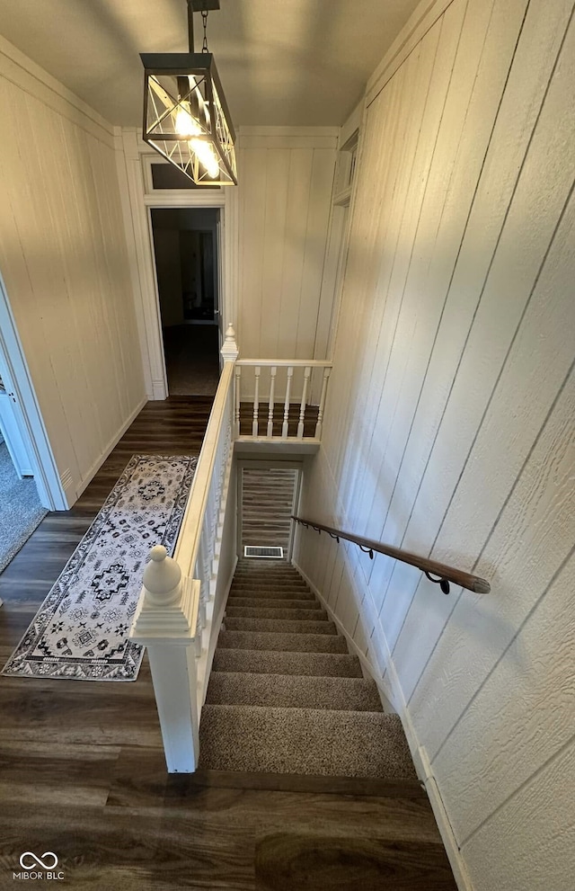 stairway featuring hardwood / wood-style floors, wooden walls, and an inviting chandelier