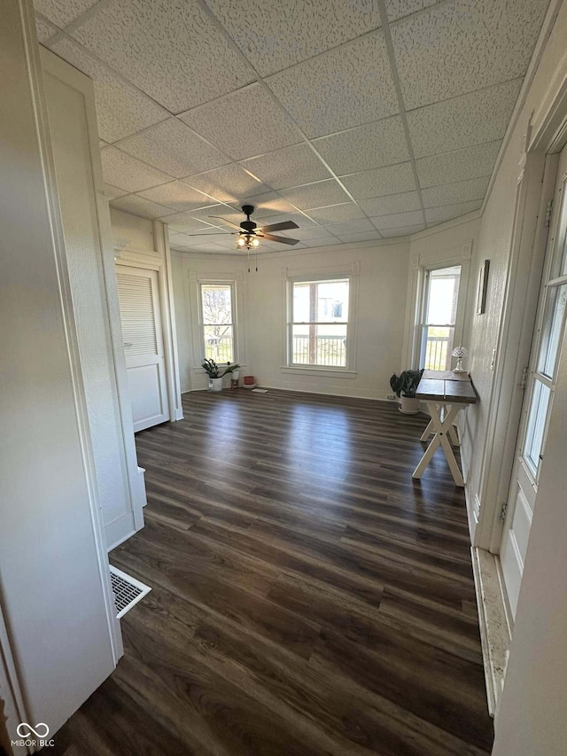 unfurnished living room with a drop ceiling, dark wood-type flooring, and ceiling fan