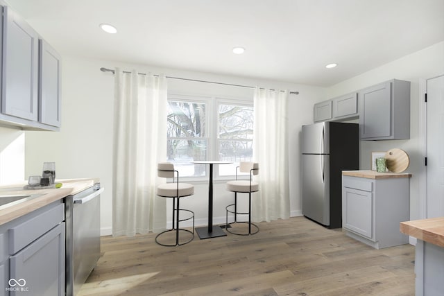 kitchen with stainless steel appliances, gray cabinets, butcher block counters, and light hardwood / wood-style floors