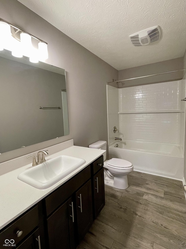 full bathroom with wood-type flooring, a textured ceiling, toilet, vanity, and bathtub / shower combination