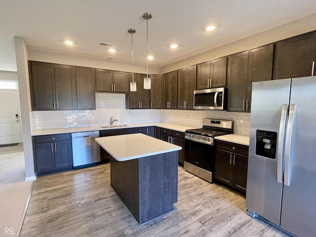 kitchen featuring sink, light wood-type flooring, decorative light fixtures, a kitchen island, and stainless steel appliances