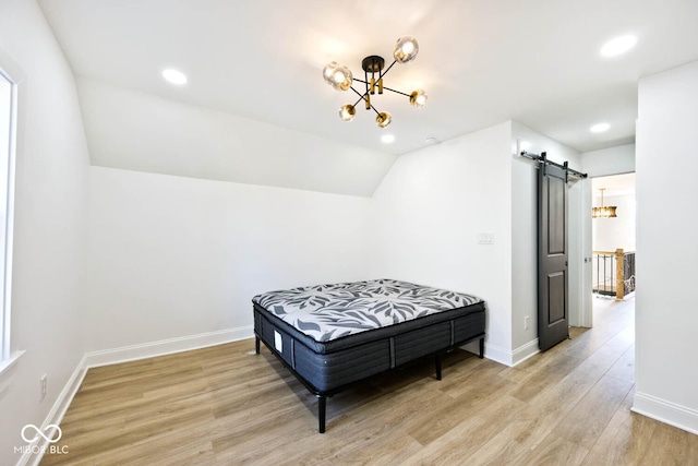 bedroom with a barn door, light hardwood / wood-style flooring, lofted ceiling, and an inviting chandelier