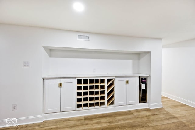 bar featuring light wood-type flooring, white cabinetry, and beverage cooler