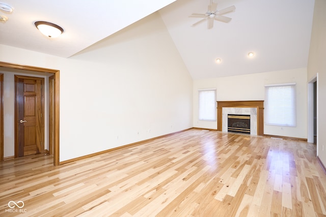 unfurnished living room featuring light wood-type flooring, high vaulted ceiling, ceiling fan, and a premium fireplace