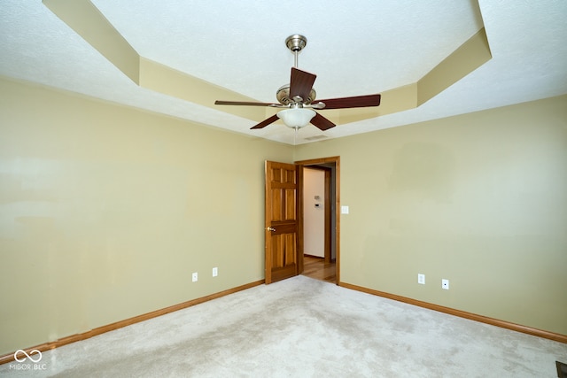 carpeted empty room featuring a textured ceiling, a tray ceiling, and ceiling fan