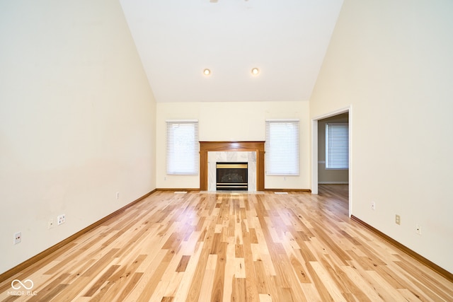 unfurnished living room with a fireplace, high vaulted ceiling, and light hardwood / wood-style flooring