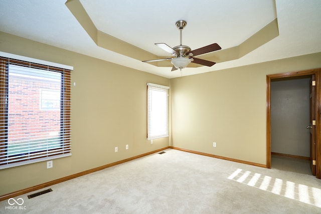 carpeted empty room with ceiling fan and a raised ceiling