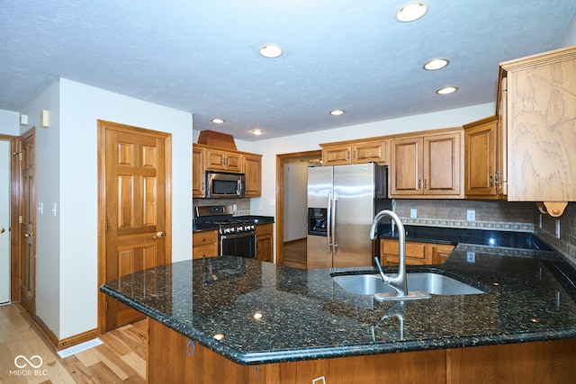 kitchen with sink, kitchen peninsula, dark stone counters, appliances with stainless steel finishes, and light wood-type flooring