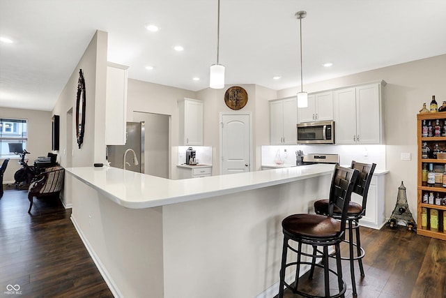 kitchen featuring hanging light fixtures, appliances with stainless steel finishes, white cabinetry, dark hardwood / wood-style flooring, and kitchen peninsula