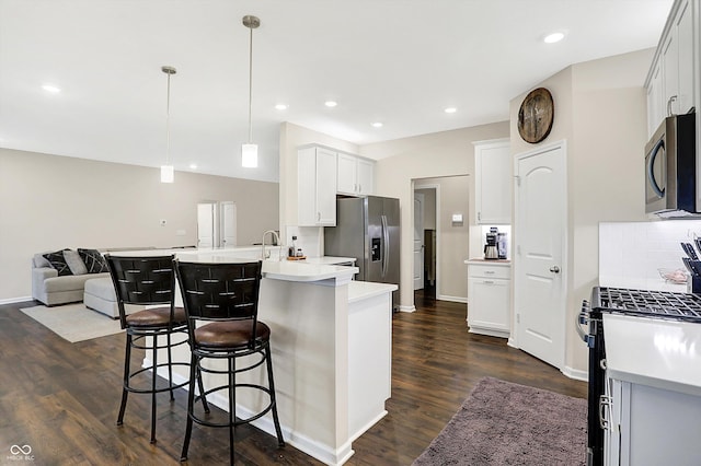 kitchen featuring kitchen peninsula, appliances with stainless steel finishes, a kitchen breakfast bar, dark hardwood / wood-style floors, and hanging light fixtures