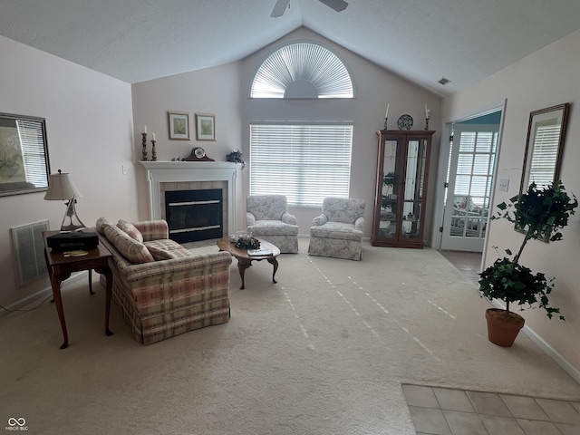 carpeted living room with ceiling fan, lofted ceiling, and a tiled fireplace