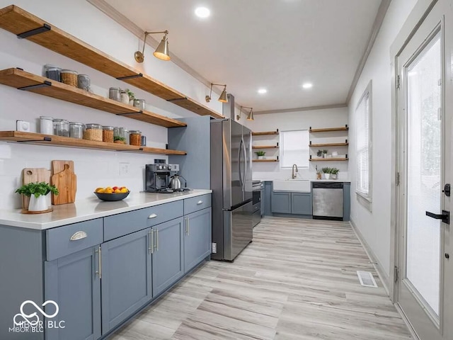 kitchen featuring sink, light hardwood / wood-style flooring, decorative backsplash, blue cabinetry, and stainless steel appliances