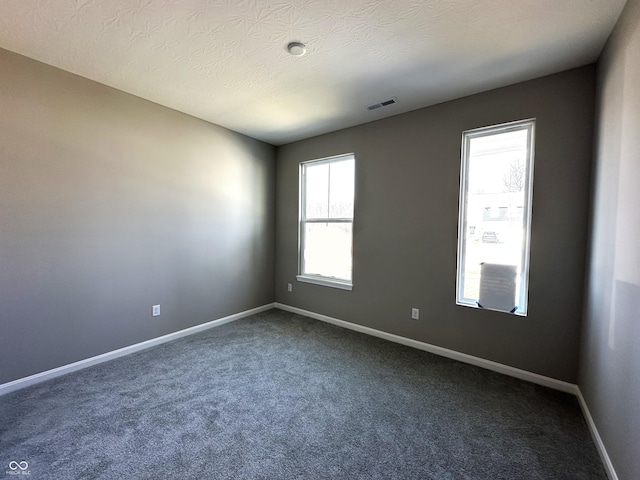 spare room featuring baseboards, visible vents, dark colored carpet, and a textured ceiling