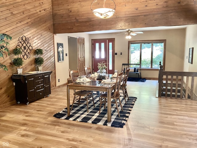 dining space with light wood finished floors, wooden walls, lofted ceiling, and baseboards