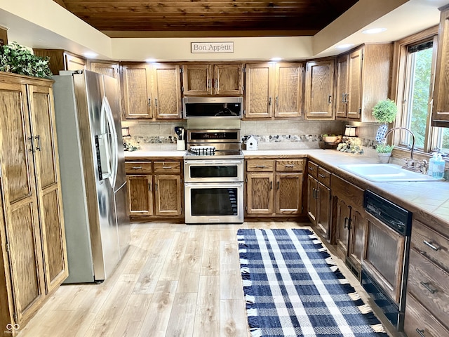 kitchen featuring tasteful backsplash, wood ceiling, light wood-type flooring, stainless steel appliances, and a sink