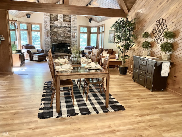 dining area featuring beam ceiling, light wood-style flooring, wooden walls, and a fireplace