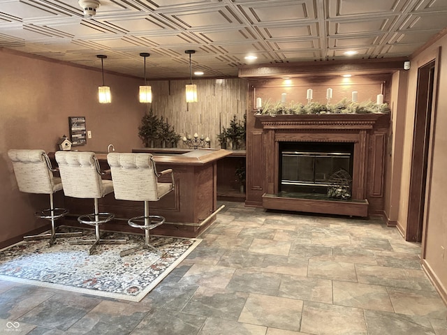 bar featuring baseboards, an ornate ceiling, indoor wet bar, hanging light fixtures, and a glass covered fireplace