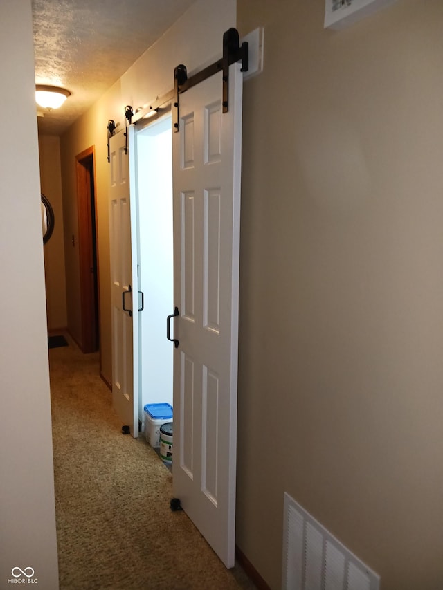 hall with a barn door, carpet, and a textured ceiling