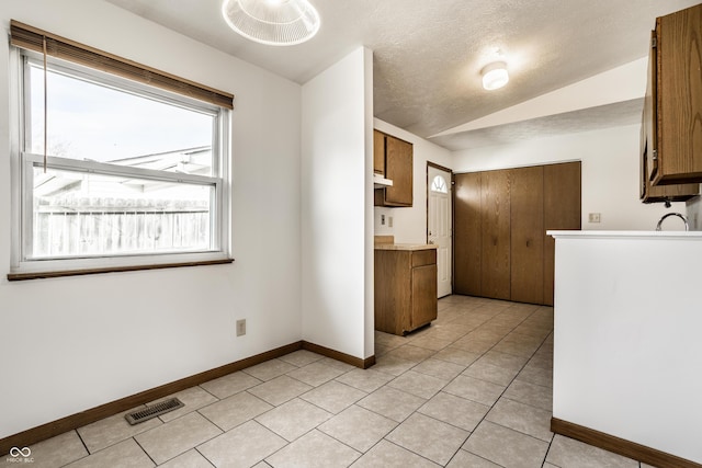 kitchen with a textured ceiling, plenty of natural light, lofted ceiling, and light tile patterned flooring