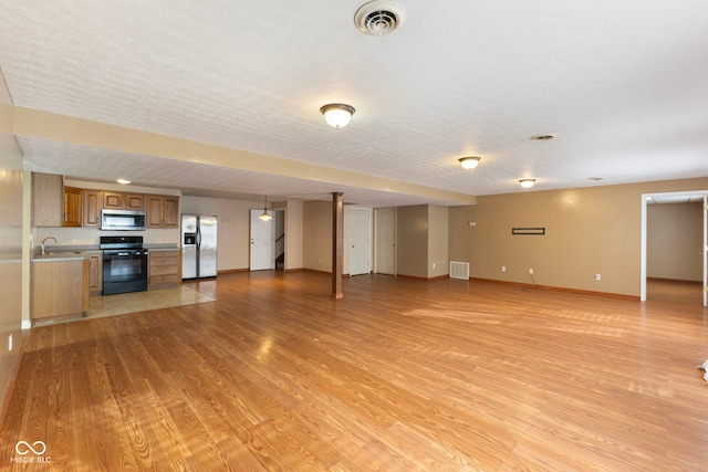 unfurnished living room featuring a textured ceiling, light wood-type flooring, and sink