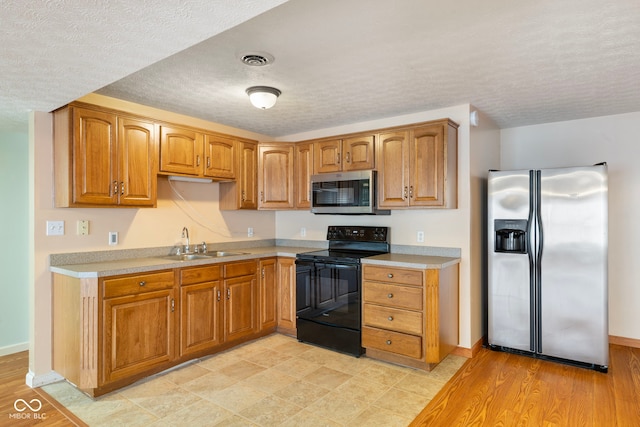 kitchen featuring a textured ceiling, sink, appliances with stainless steel finishes, and light hardwood / wood-style flooring