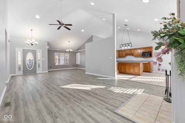 unfurnished living room with ceiling fan with notable chandelier, light hardwood / wood-style floors, and high vaulted ceiling