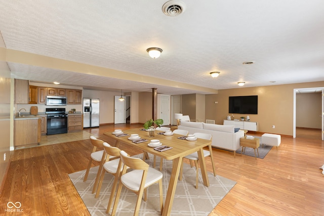 dining area featuring a textured ceiling, light hardwood / wood-style flooring, and sink