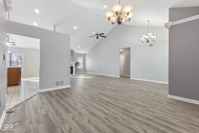 unfurnished living room featuring high vaulted ceiling, light hardwood / wood-style floors, and ceiling fan with notable chandelier