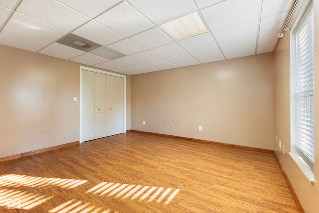 unfurnished bedroom with a drop ceiling, light hardwood / wood-style floors, and a closet