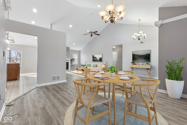 dining space with ceiling fan with notable chandelier, light wood-type flooring, and high vaulted ceiling