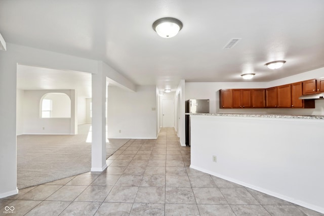 kitchen with stainless steel fridge, light colored carpet, and light stone counters