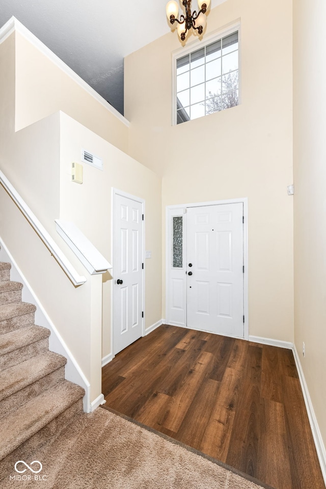 foyer entrance with wood-type flooring, a towering ceiling, and an inviting chandelier