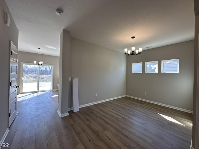 empty room featuring a chandelier, dark wood-style floors, a textured ceiling, and baseboards