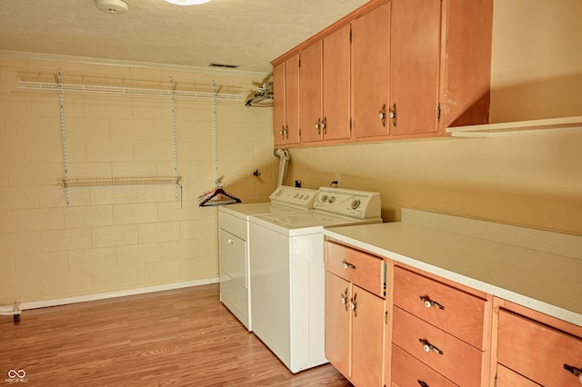 laundry room featuring washer and dryer, cabinets, a textured ceiling, and light hardwood / wood-style flooring