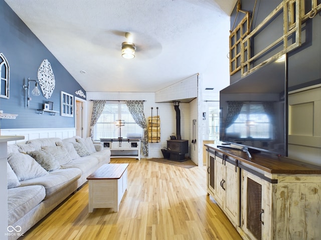 living room featuring a wood stove, vaulted ceiling, ceiling fan, light wood-type flooring, and a textured ceiling