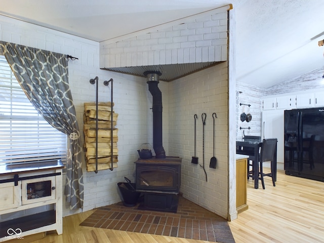 room details with a wood stove, black refrigerator with ice dispenser, and hardwood / wood-style floors