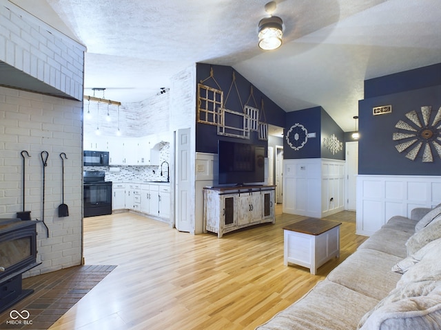 living room with a wood stove, light hardwood / wood-style floors, high vaulted ceiling, and sink