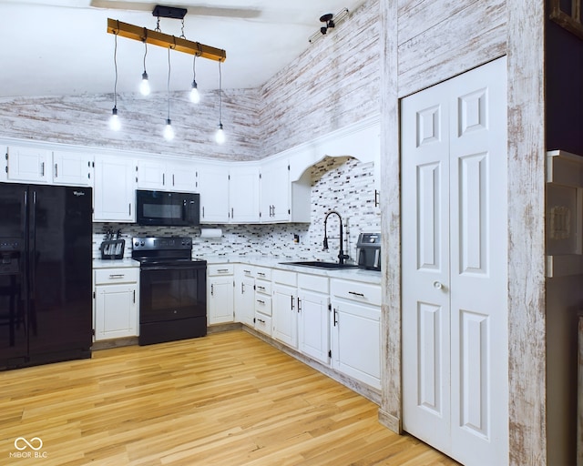 kitchen with a towering ceiling, sink, black appliances, light hardwood / wood-style flooring, and white cabinets