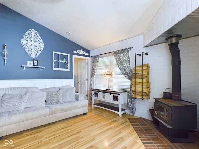 living room with wood-type flooring, vaulted ceiling, and a wood stove