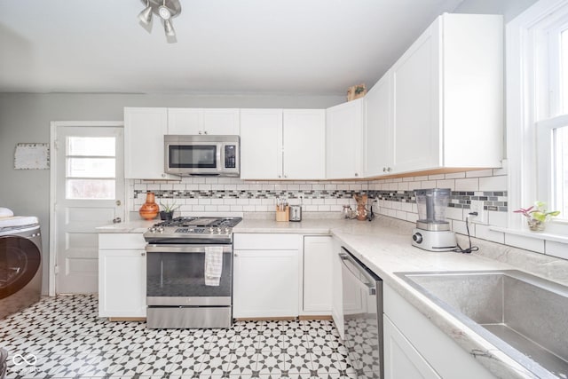 kitchen featuring sink, decorative backsplash, washer / dryer, white cabinetry, and stainless steel appliances