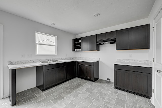 kitchen featuring a textured ceiling, light stone countertops, and sink