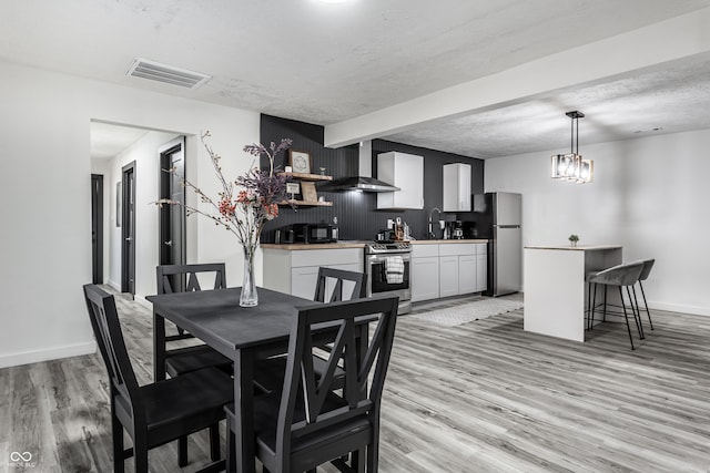 dining area featuring beam ceiling, sink, a textured ceiling, and light wood-type flooring