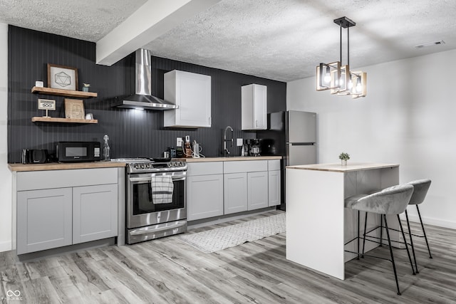 kitchen featuring wall chimney range hood, white cabinetry, a breakfast bar, and stainless steel range oven