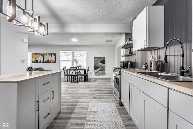 kitchen featuring white cabinets, sink, hanging light fixtures, a textured ceiling, and light hardwood / wood-style floors